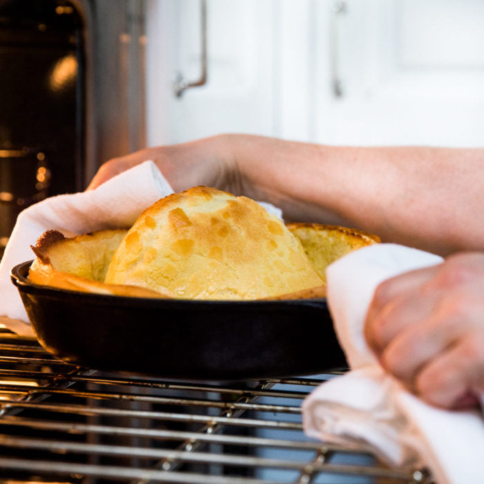Einkorn Dutch baby pancake puffing in a cast-iron skillet as hands remove it from an oven rack