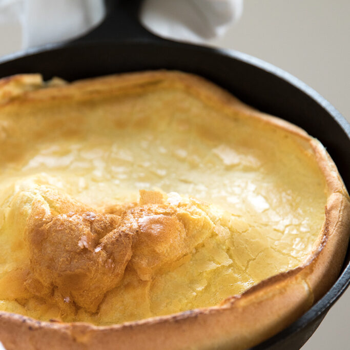 Close-up of an Einkorn Dutch baby pancake in a cast-iron skillet showing a puffed center and crispy golden edges