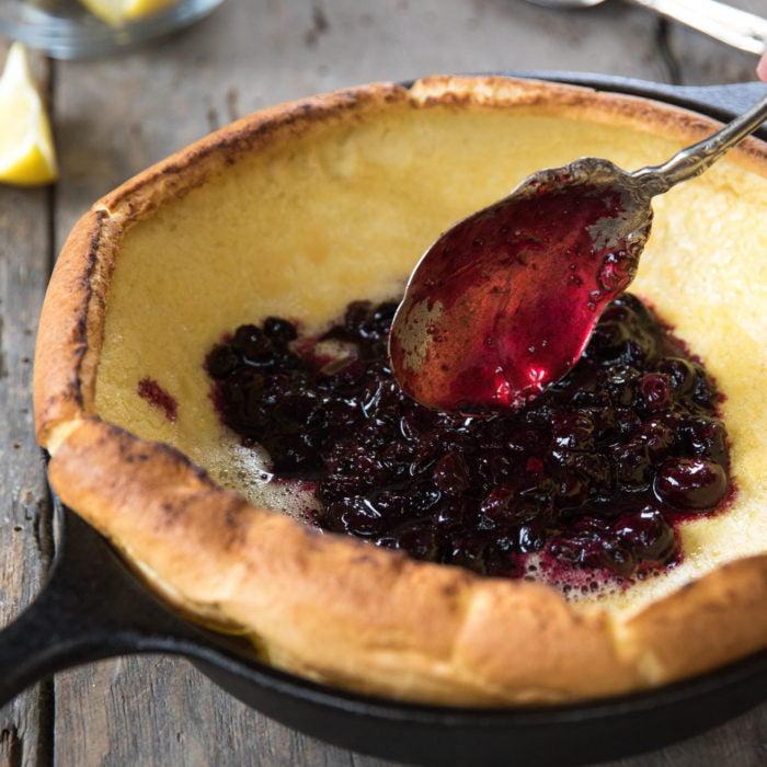 Overhead view of an Einkorn Dutch baby pancake in a cast-iron skillet topped with blueberry compote