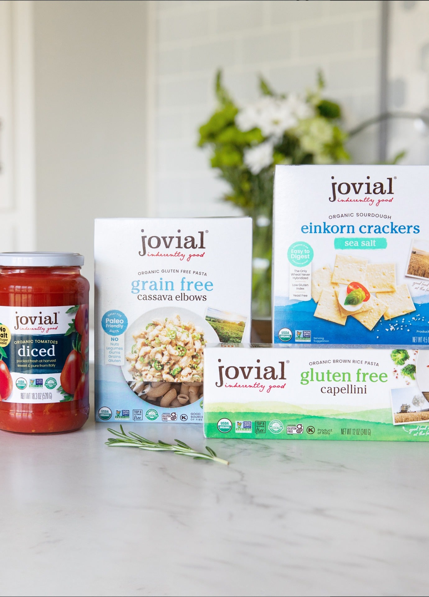 Front of Jovial product assortment showing organic gluten-free pasta, einkorn crackers, and diced tomatoes on marble counter