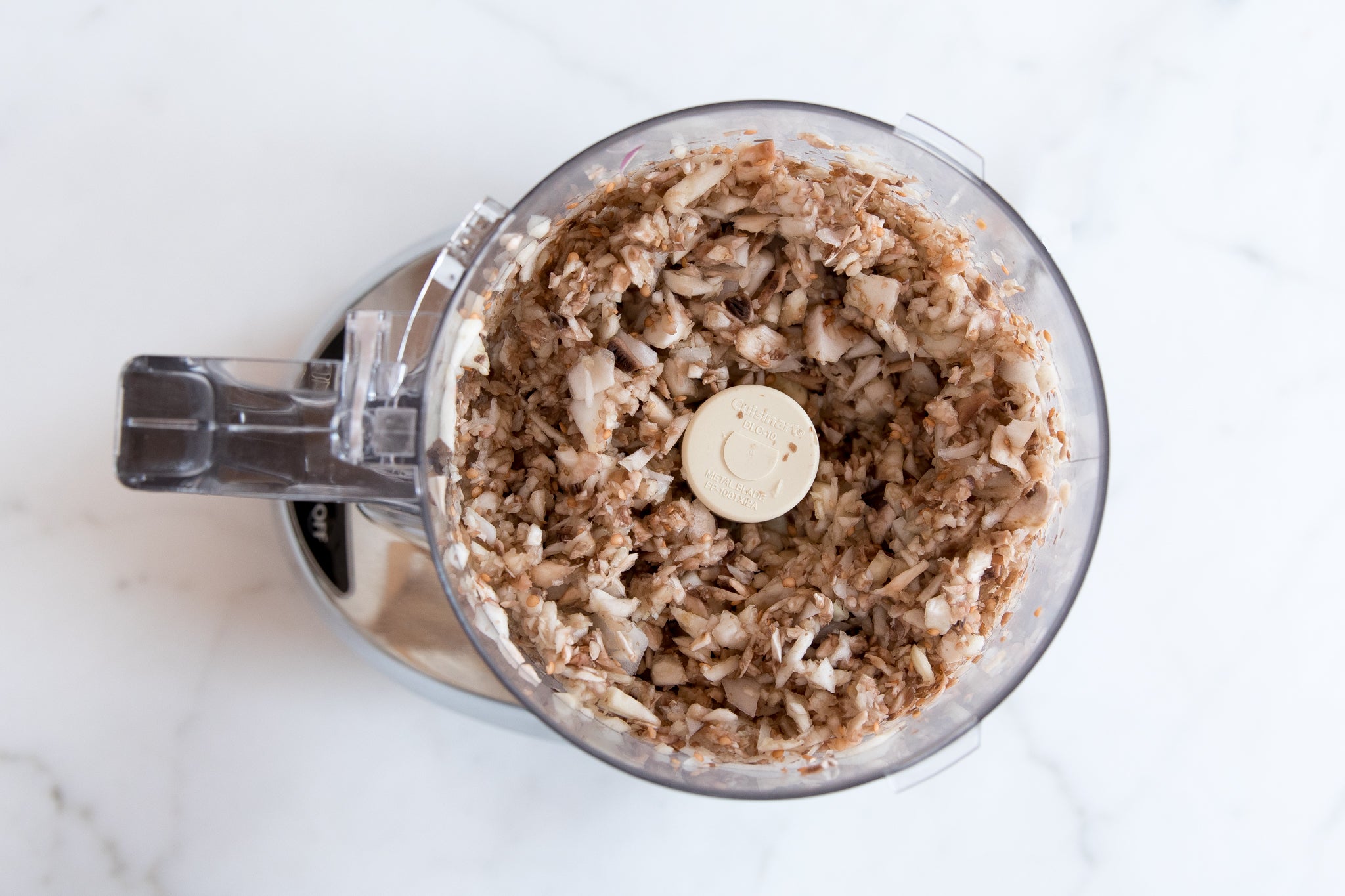 Chopped eggplant and mushrooms pulsed in a food processor bowl for vegan mushroom bolognese on a white countertop