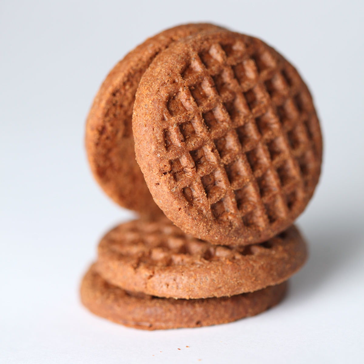 Close up of three Organic Einkorn Crispy Cocoa Cookies stacked showing crispy texture and grid pattern on light background