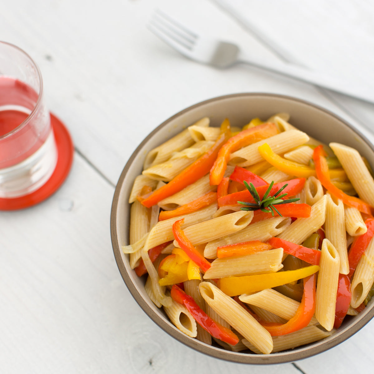Bowl of cooked Organic Einkorn traditional penne with sliced carrots and rosemary on a white table
