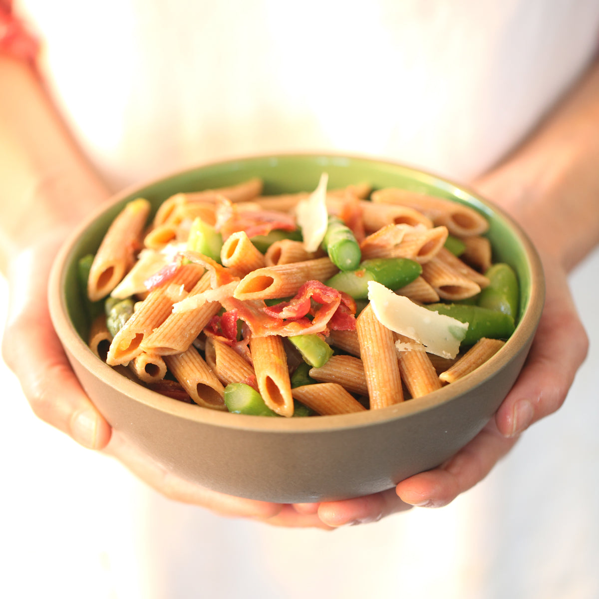 Bowl of cooked Organic Einkorn whole wheat penne garnished with green onions, held in hands