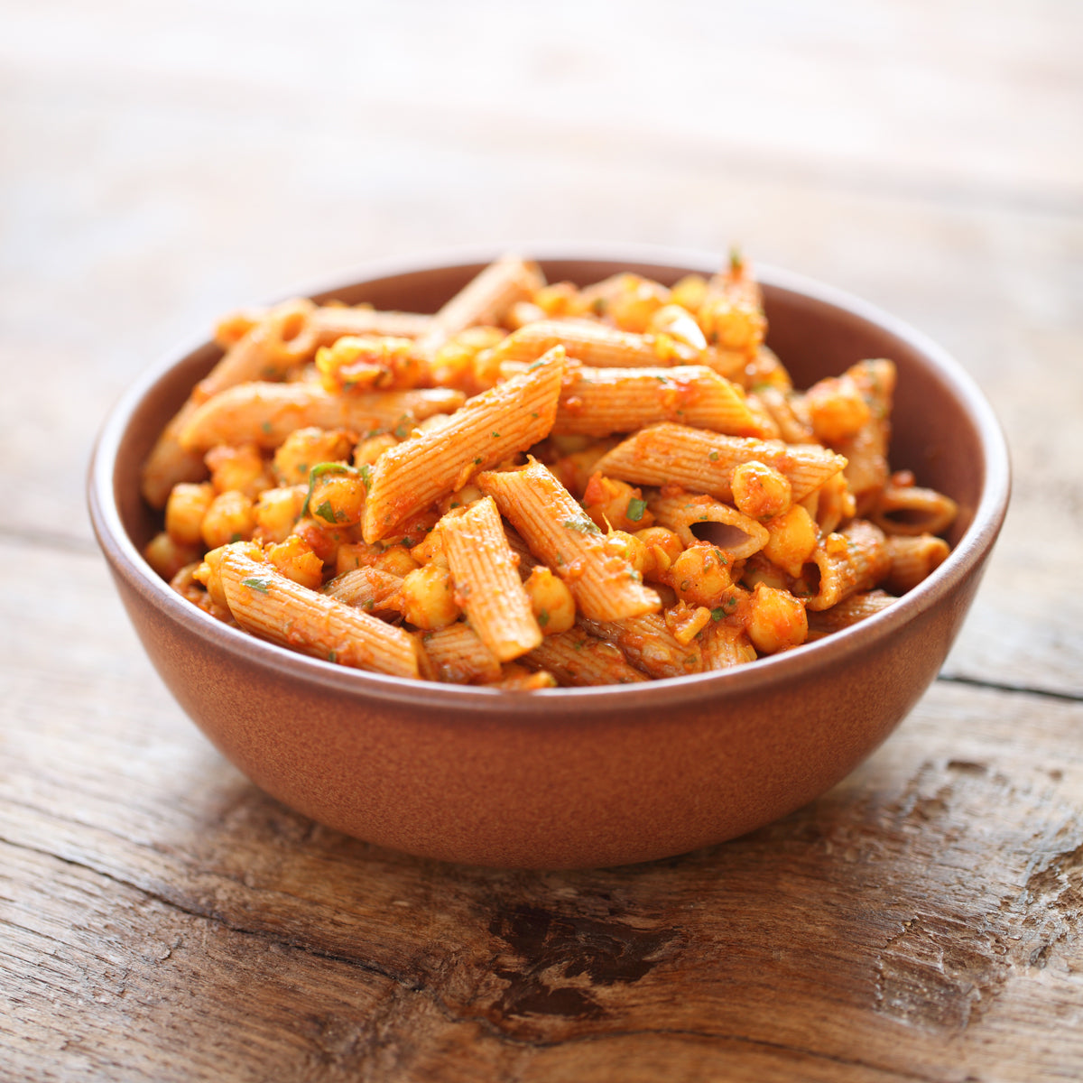 Bowl of cooked organic Einkorn whole wheat penne with chickpeas in tomato sauce on a wooden table
