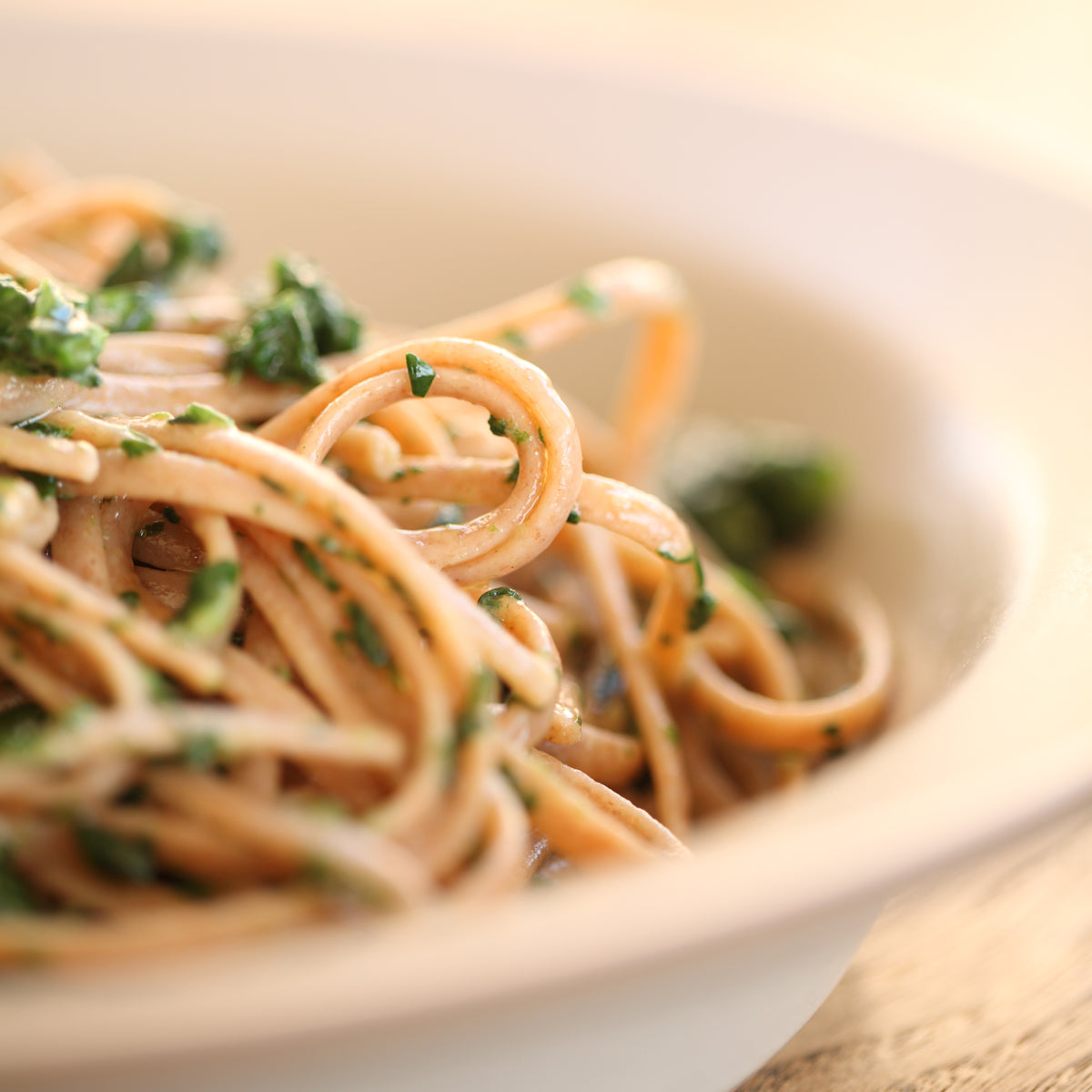Cooked organic einkorn whole wheat spaghetti tossed with chopped herbs in a shallow white bowl