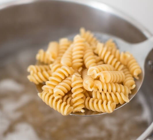 Close-up of Einkorn fusilli showing spiral ridges and golden color in a metal slotted spoon over simmering water