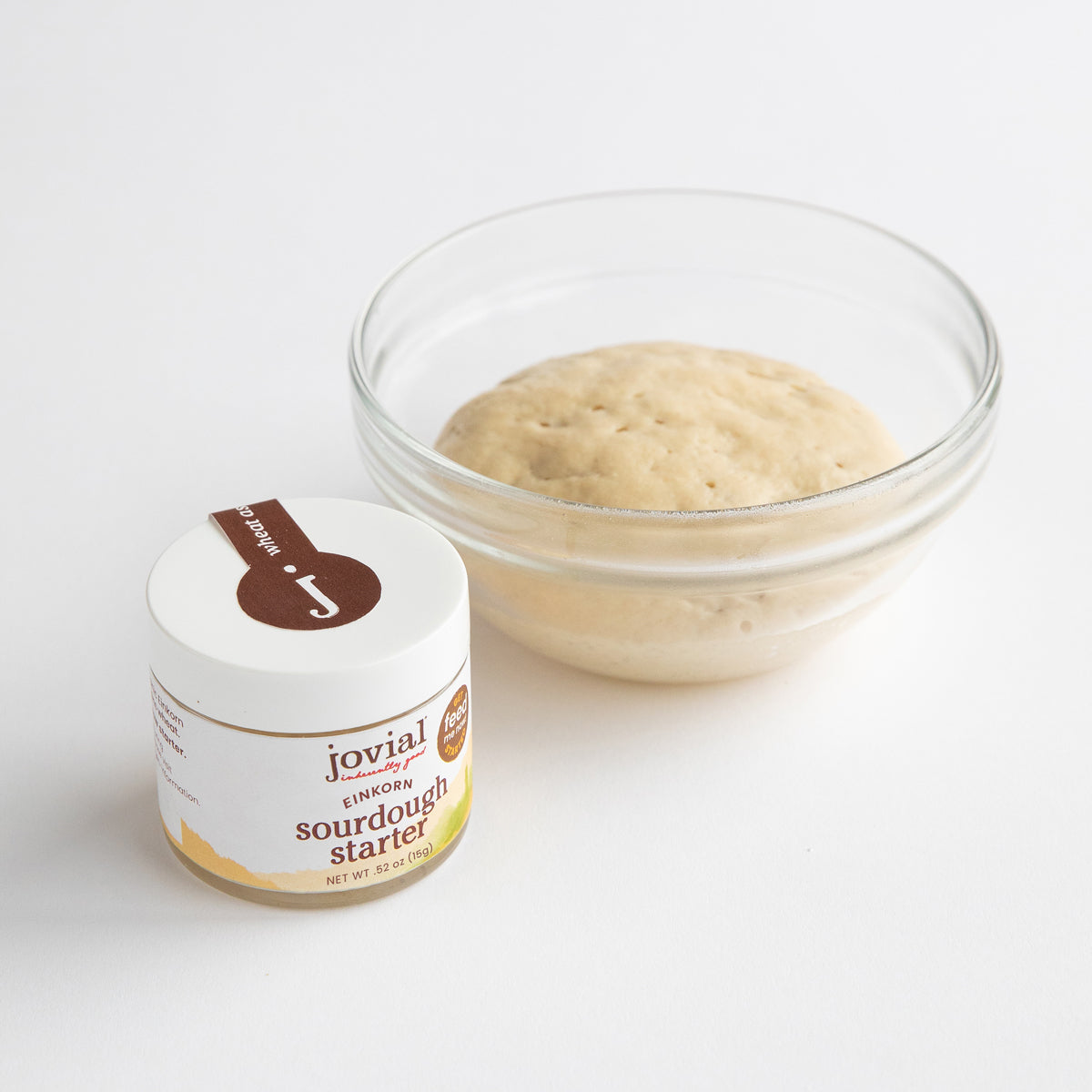 Front view of Jovial Einkorn sourdough starter jar beside a glass bowl of risen starter on a white background