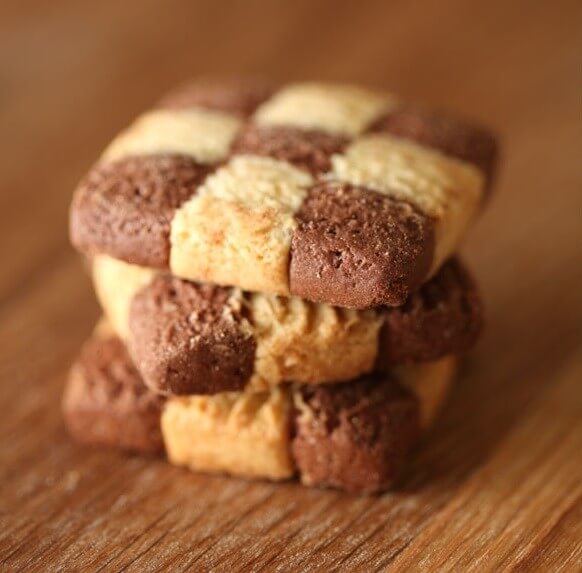 Close-up of stacked Organic Einkorn checkerboard cookies showing chocolate and vanilla shortbread squares on a wooden surface