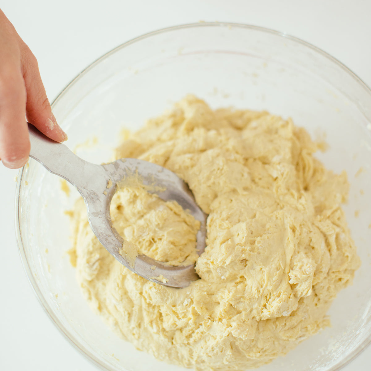 Top-down view of Einkorn Kneading Tool showing polished stainless steel blade with center hole mixing dough in glass bowl