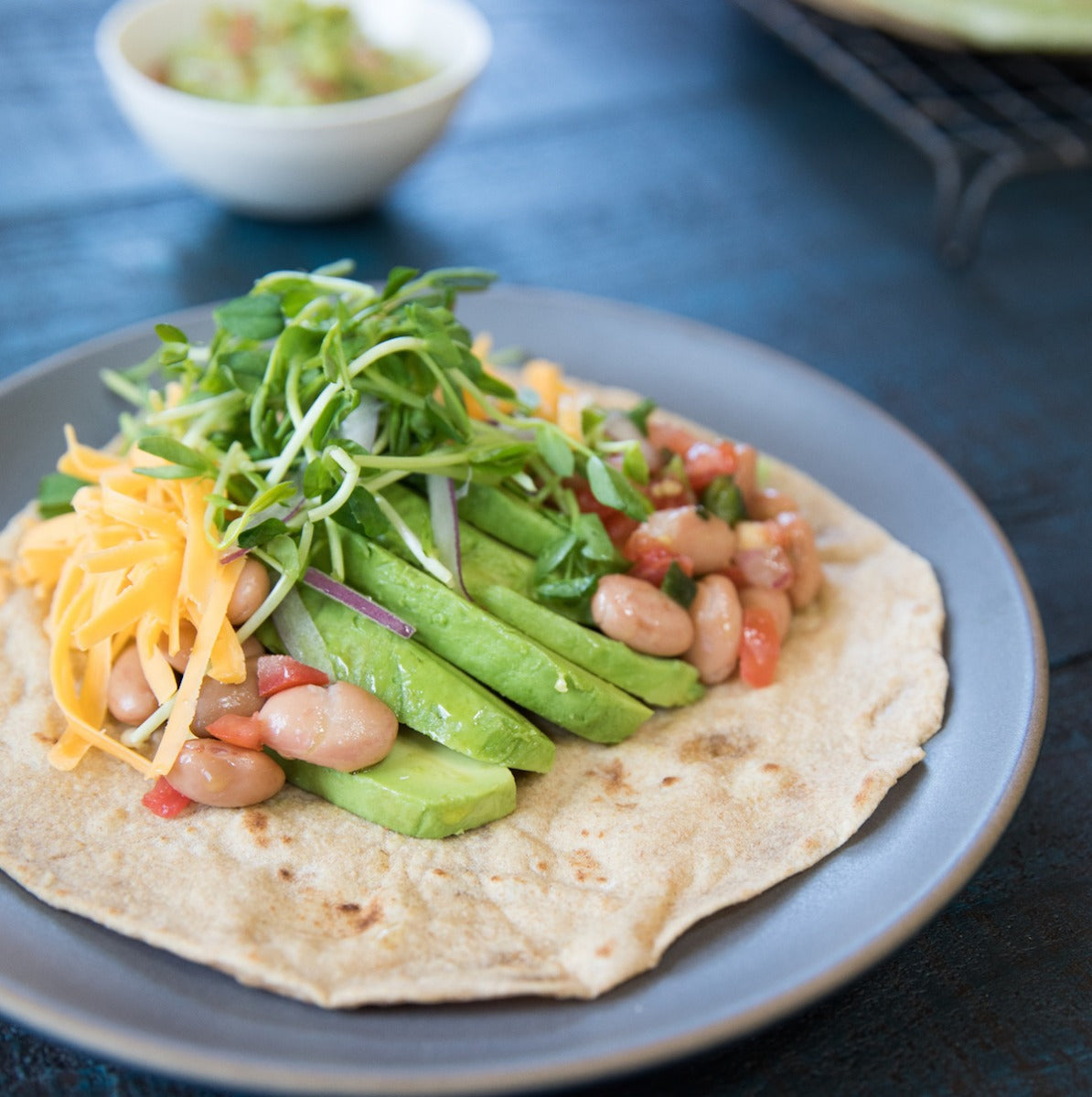 Spinach einkorn tortillas on a plate topped with microgreens and avocado as a serving suggestion