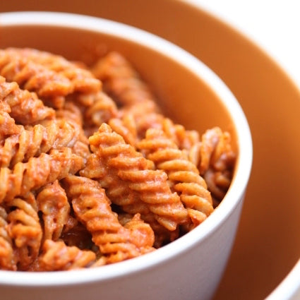 Cooked Einkorn whole wheat fusilli tossed in tomato sauce in an orange bowl
