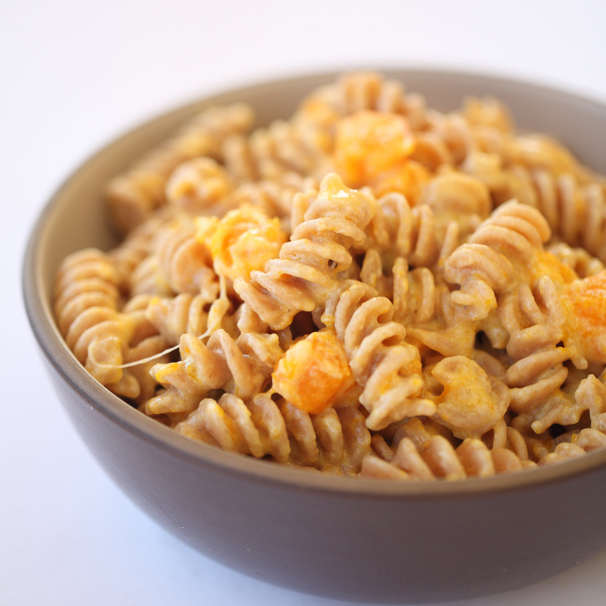 Bowl of cooked organic Einkorn whole wheat fusilli tossed with grated cheese in a beige bowl on a light background
