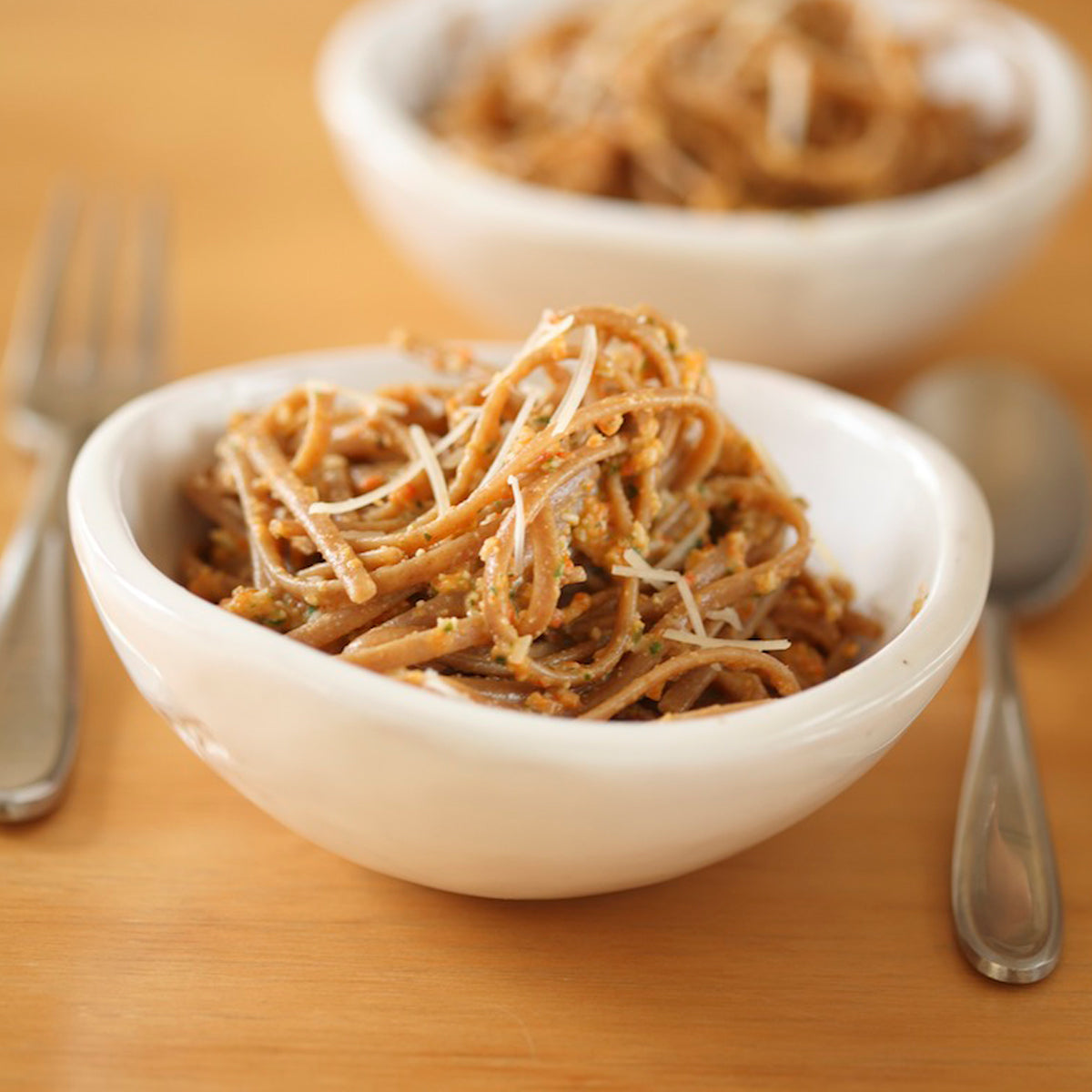Cooked Organic Einkorn whole wheat linguine in a white bowl topped with roasted red peppers and grated cheese on a wooden table