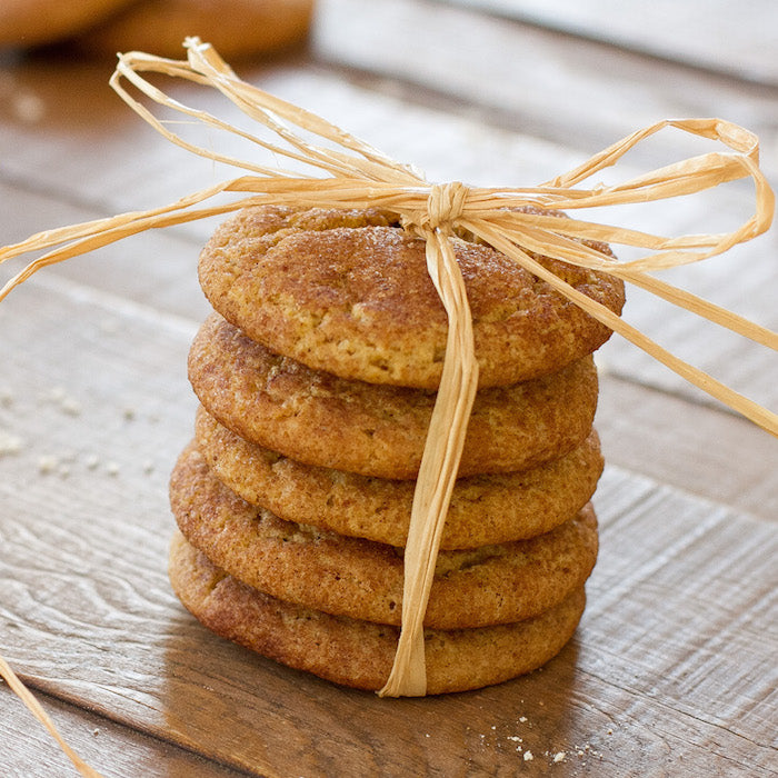 Close-up of stacked einkorn snickerdoodle cookies tied with raffia, showing cinnamon-sugar coating on a wooden tabletop