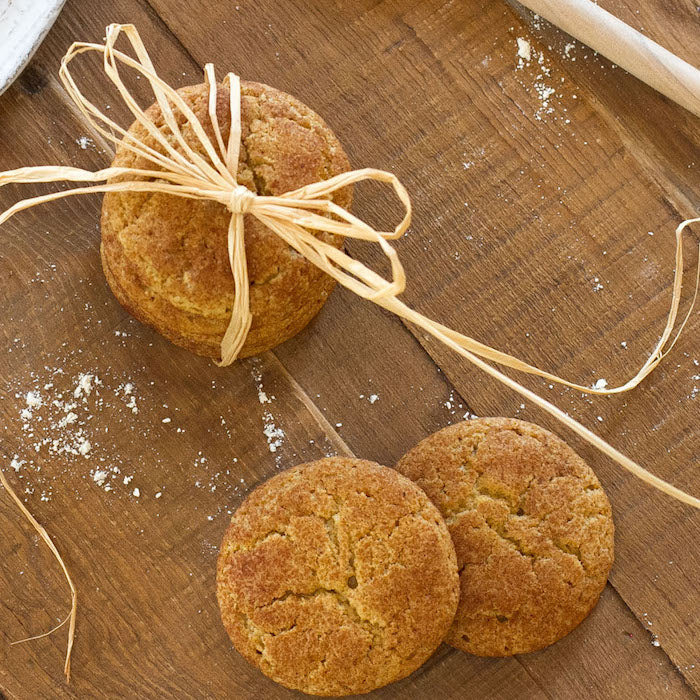 Overhead view of three einkorn snickerdoodle cookies, one tied with raffia, on a wooden board dusted with flour
