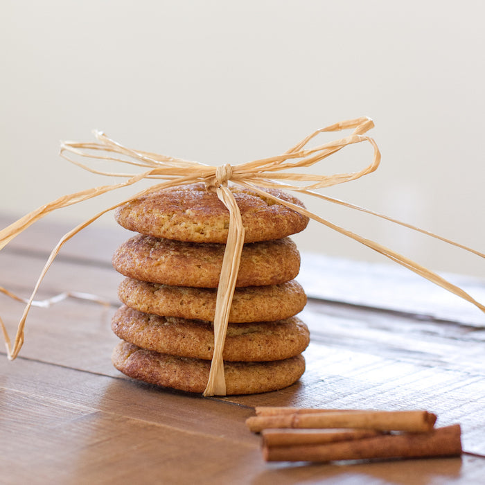 Front view of stacked einkorn snickerdoodle cookies tied with raffia ribbon, cinnamon sticks on wooden table