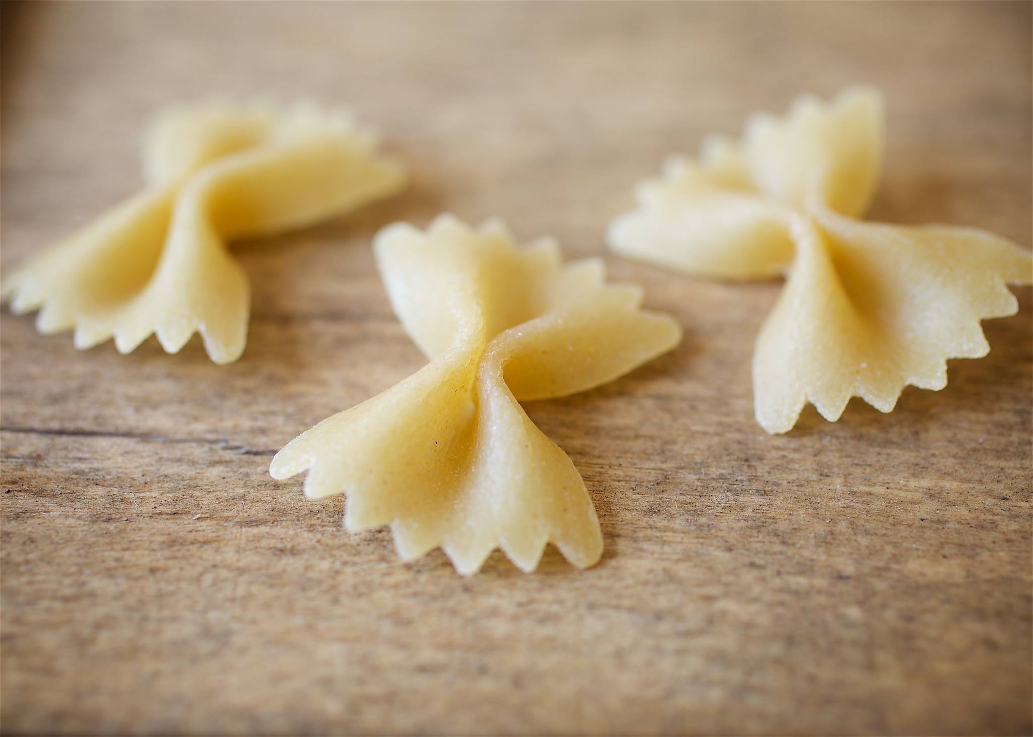 Close-up of Organic Sourdough Farfalle showcasing coarse bronze-die texture and bow-tie shape on a wooden surface