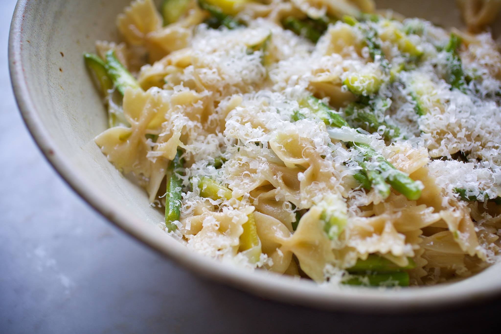 Bowl of organic sourdough farfalle tossed with zucchini, asparagus, and grated cheese in a ceramic bowl