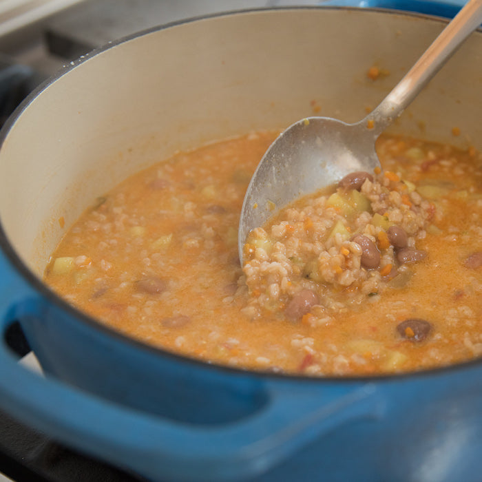 Pot of farro and bean soup being ladled from a blue Dutch oven on the stovetop
