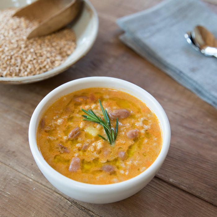 Overhead view of farro bean soup with beans and wheat berries, garnished with rosemary and olive oil on a wooden table
