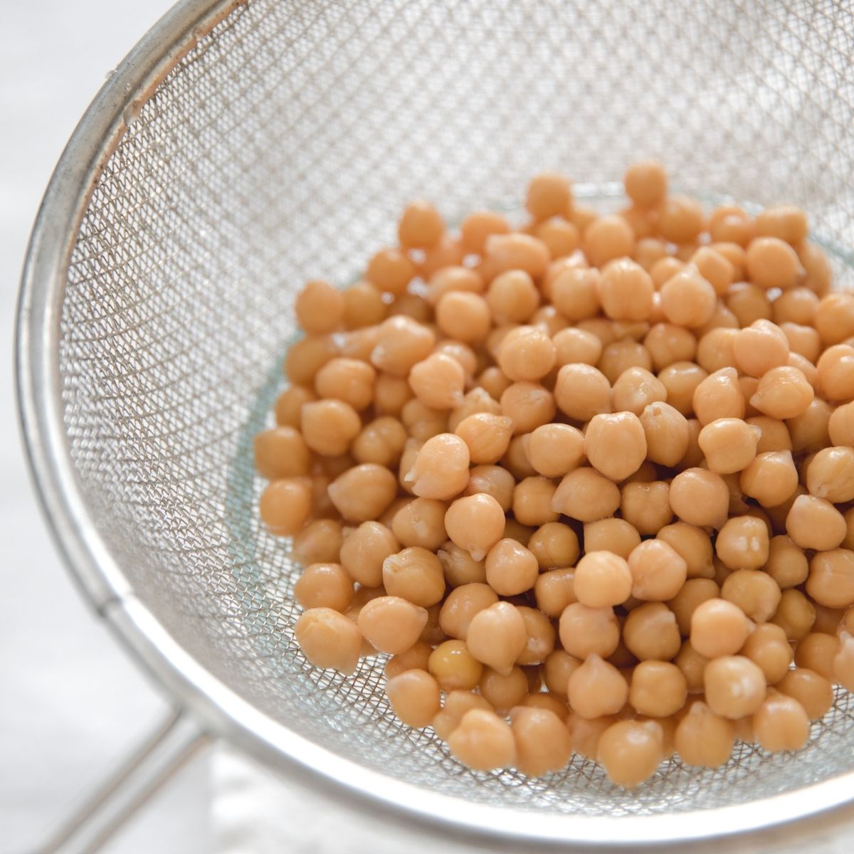 Close-up of Organic Chickpeas showcasing firm cooked beans in a metal strainer over a white background