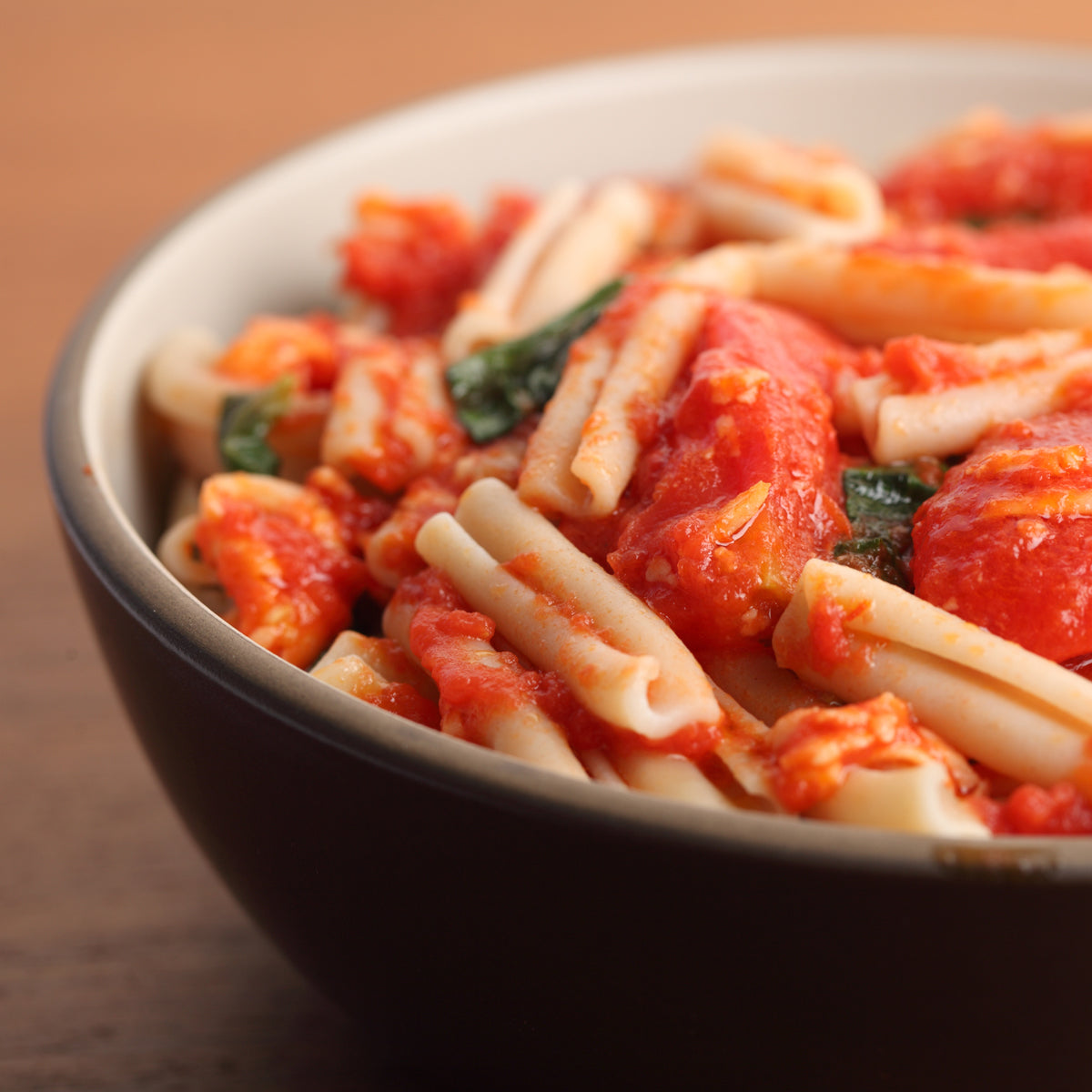 Bowl of organic brown rice caserecce in garlicky tomato sauce with basil