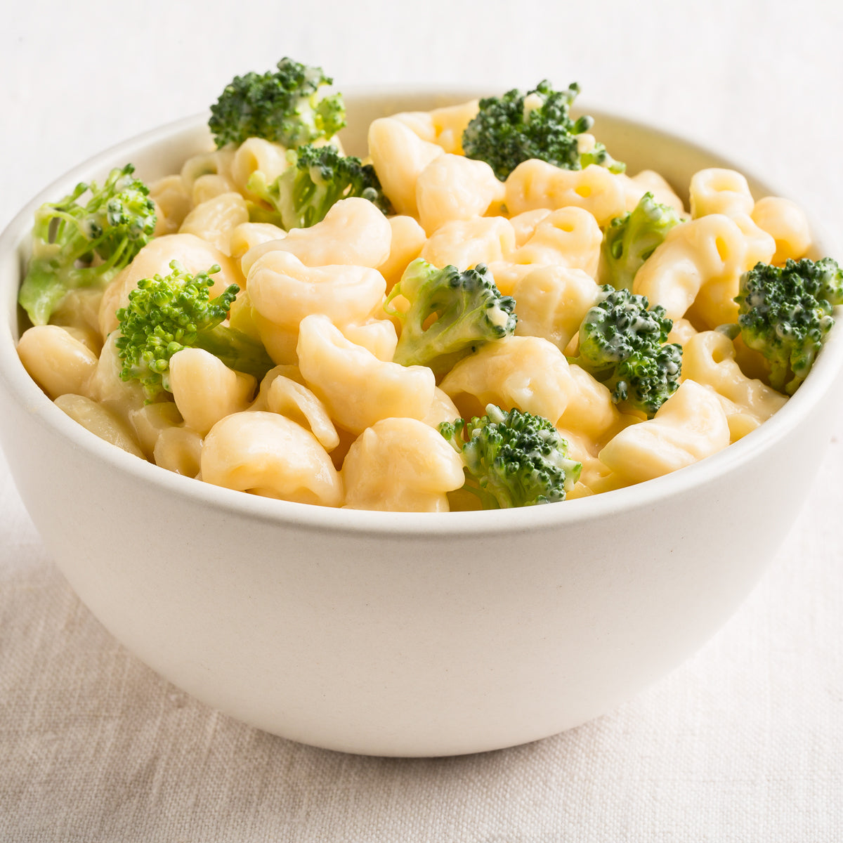 Bowl of cooked organic gluten free brown rice elbow pasta with broccoli on a light wood table