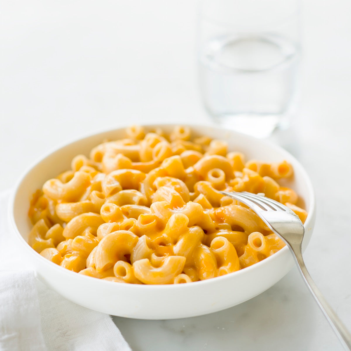 Close-up of Organic Gluten Free Brown Rice Elbows in white bowl with fork, highlighting elbow shape and firm texture