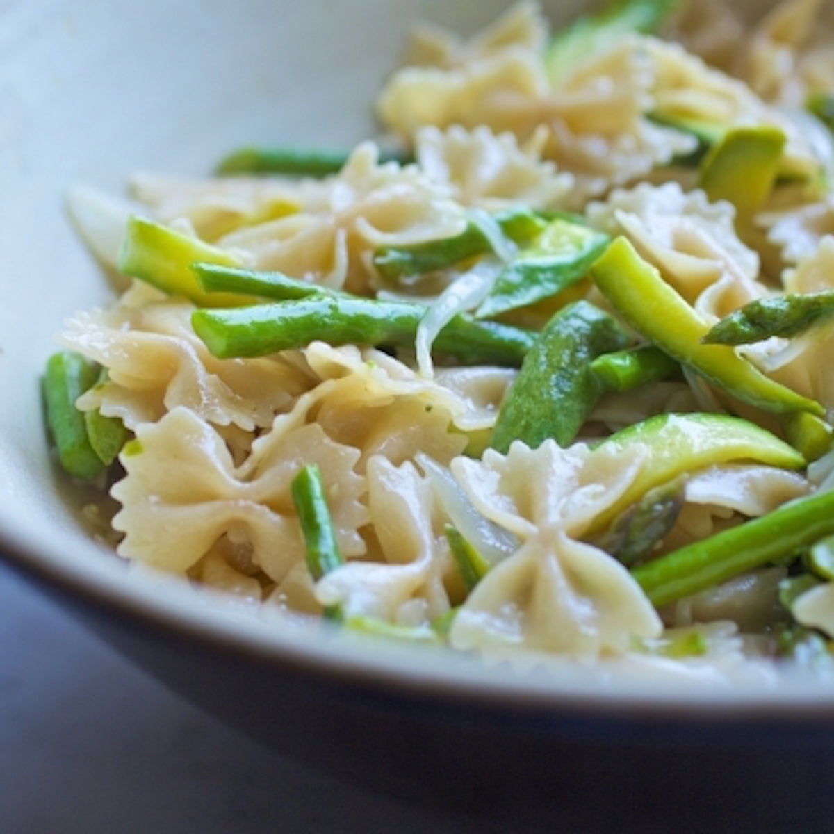 Bowl of cooked organic brown rice farfalle tossed with zucchini ribbons and grated cheese in a shallow ceramic bowl