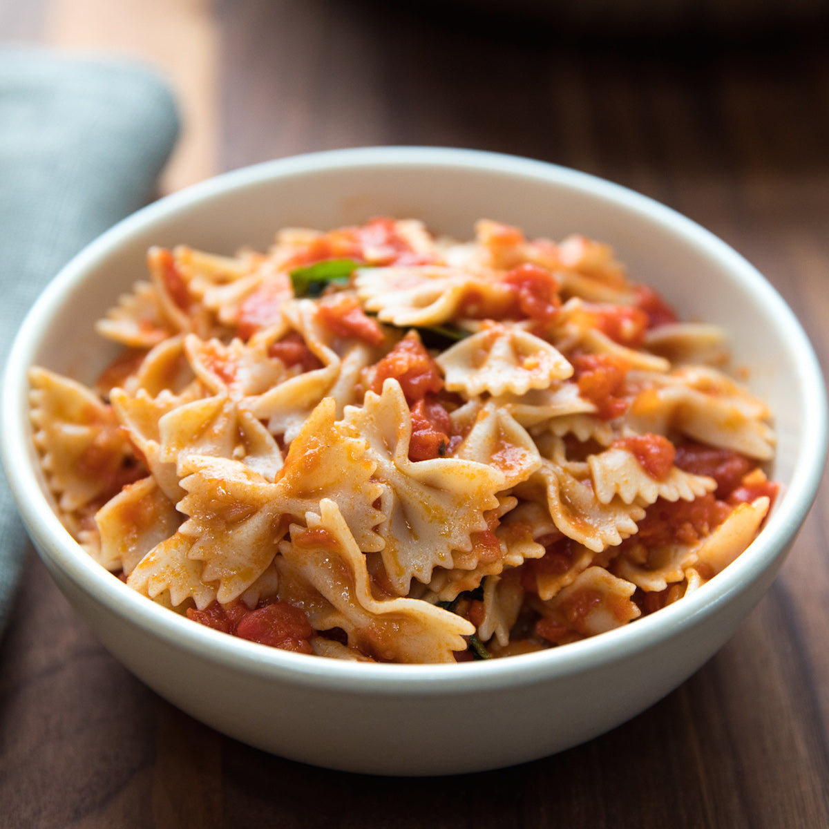 Bowl of cooked organic gluten-free brown rice farfalle tossed in marinara sauce on a wooden table