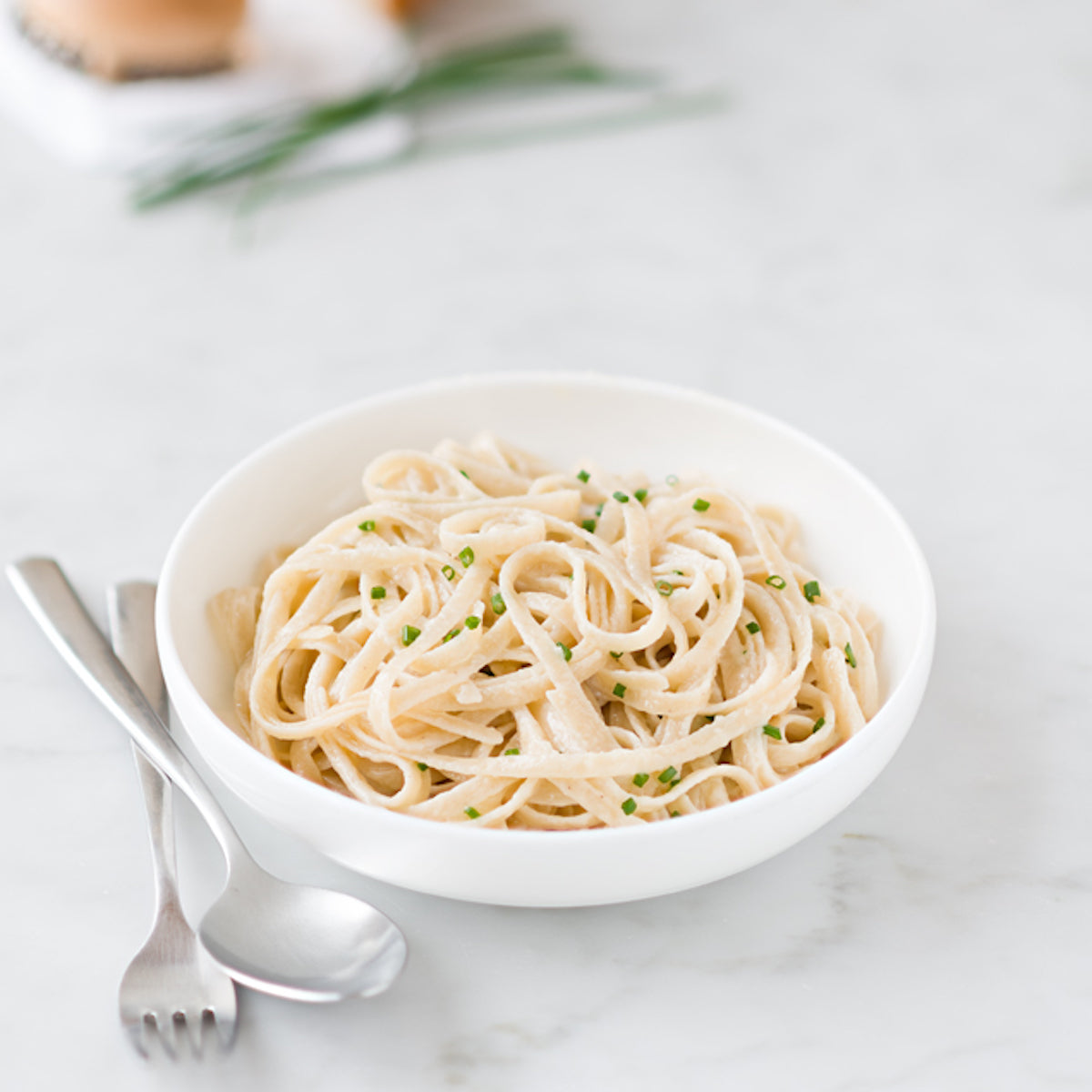 Bowl of organic gluten-free brown rice fettuccine in a creamy sauce, garnished with chopped chives on a marble surface