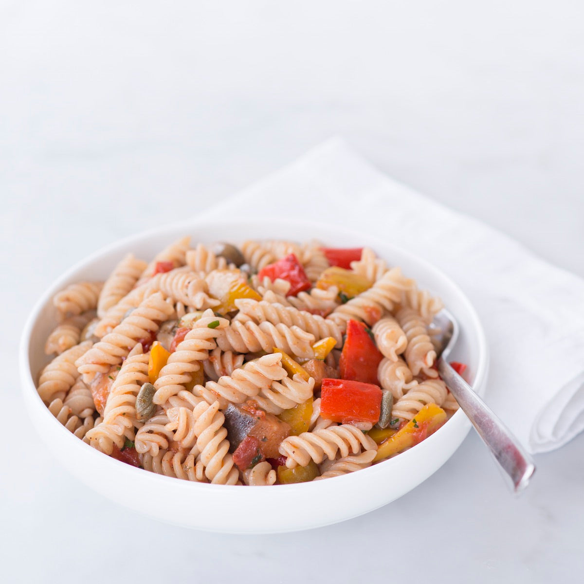 Bowl of organic brown rice fusilli pasta tossed with cherry tomatoes and herbs on a white napkin