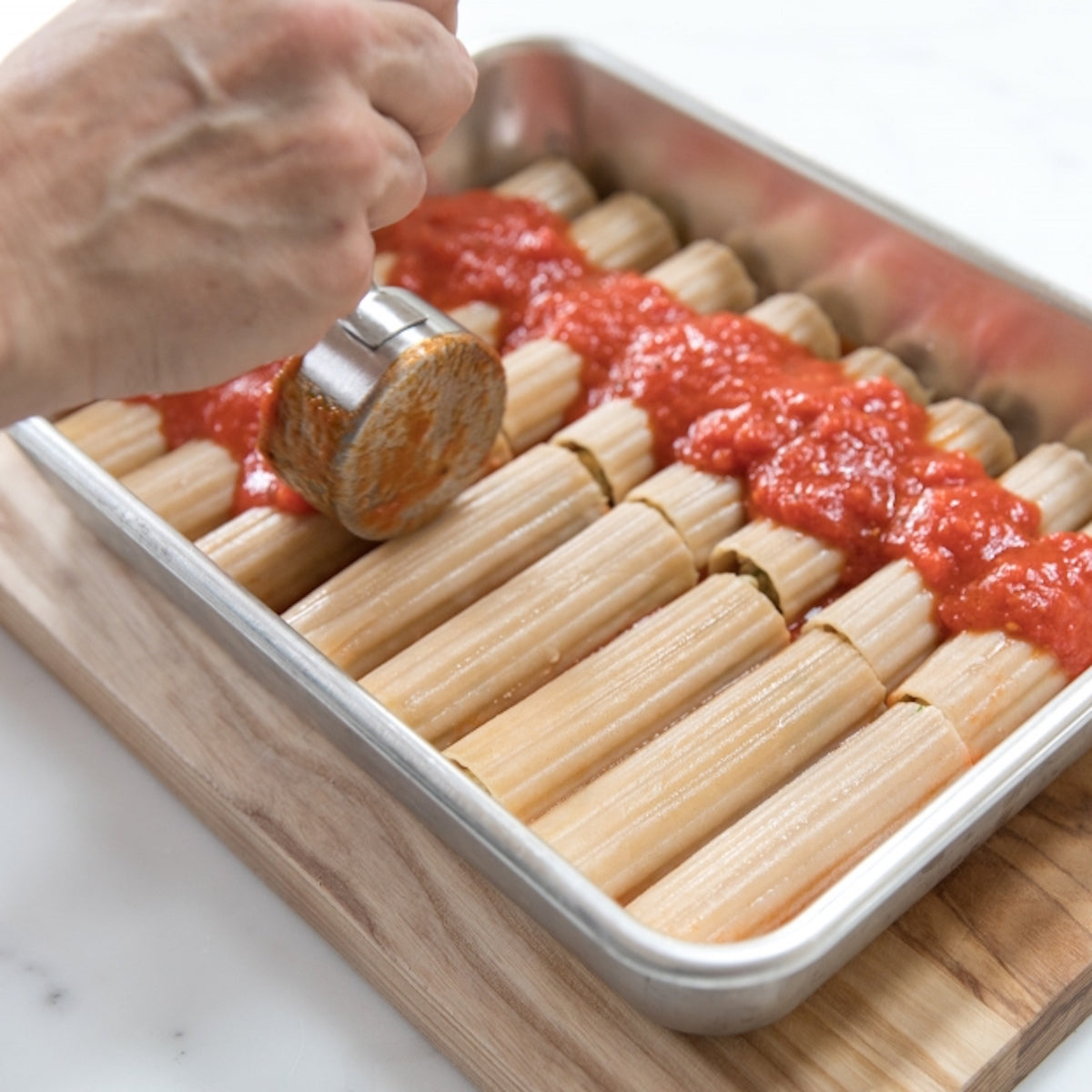 Close up of Organic Gluten Free Brown Rice Manicotti showing pasta tubes in a baking dish being topped with tomato sauce