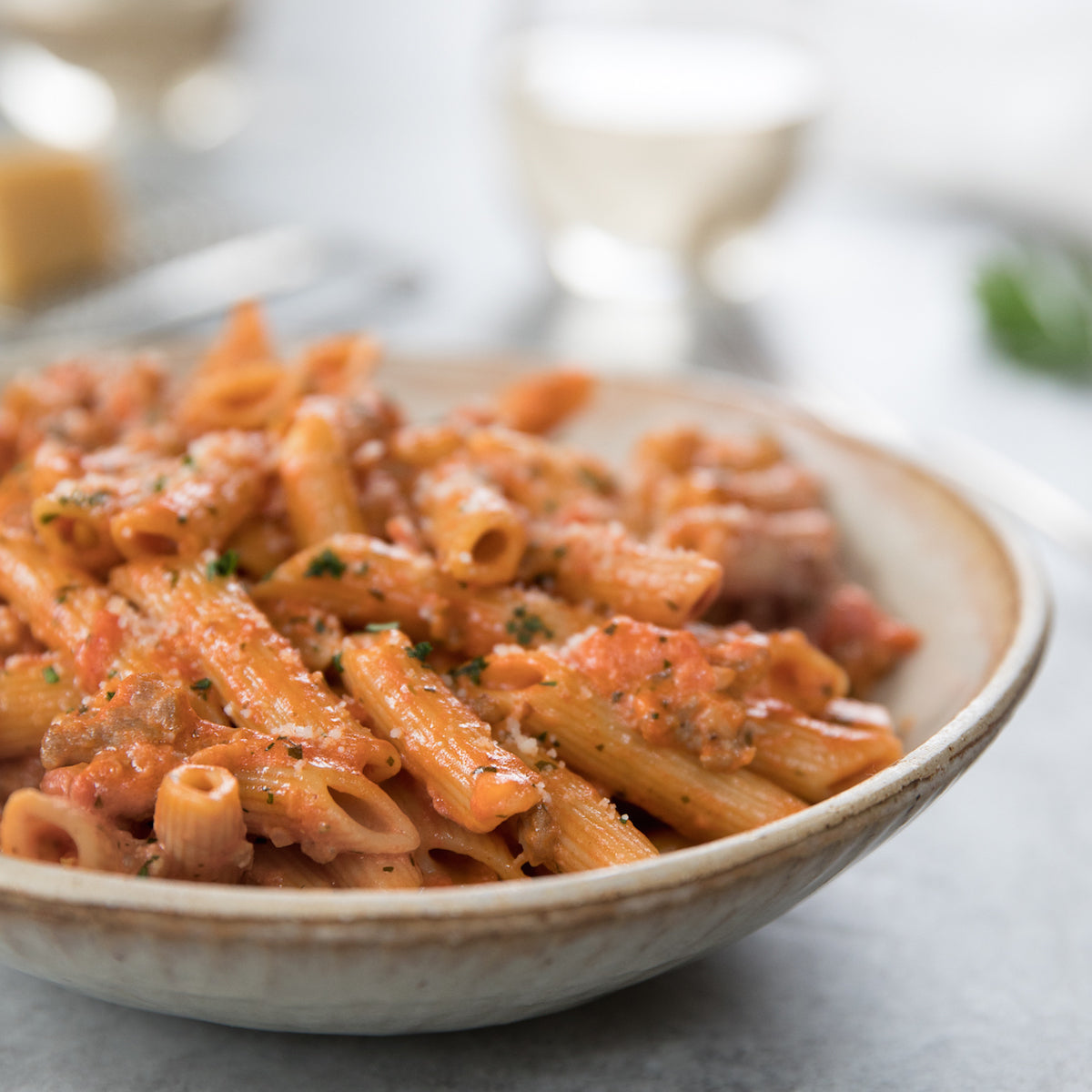 Bowl of gluten-free brown rice penne rigate in tomato cream sauce with sausage and grated cheese on a table