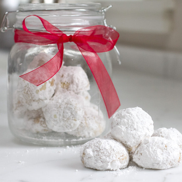 Close up of Einkorn walnut snowball cookies dusted with powdered sugar beside a glass jar tied with a red ribbon