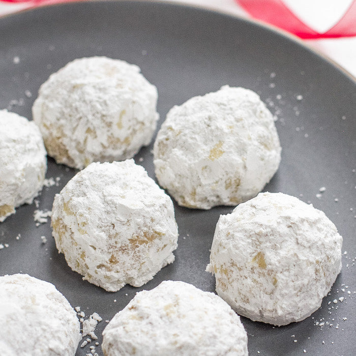 Close-up of Einkorn walnut snowball cookies showing powdered sugar coating and chopped walnuts on a gray plate