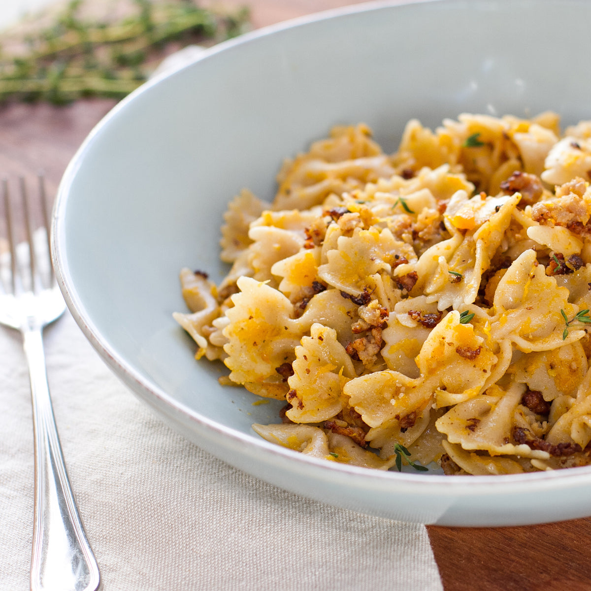 Bowl of organic gluten-free brown rice farfalle tossed with roasted butternut squash and breadcrumbs, served in a white bowl with fork