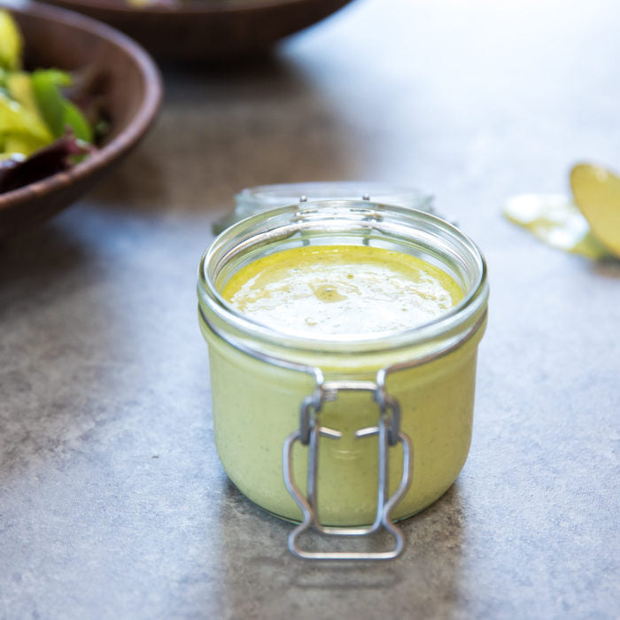 Front view of jar of green goddess salad dressing showing creamy green texture in a glass clamp jar on a gray countertop