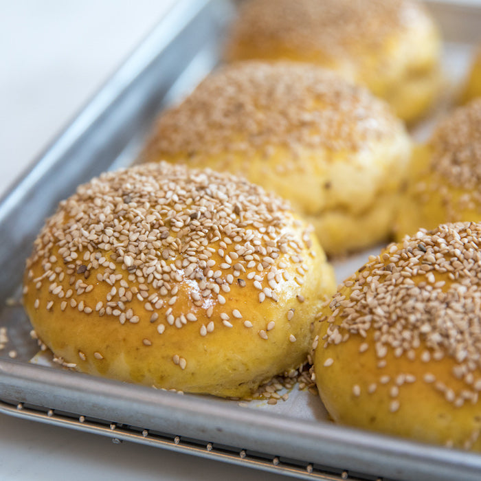 Close-up of Einkorn hamburger buns showcasing golden crust and sesame seeds on a metal baking sheet
