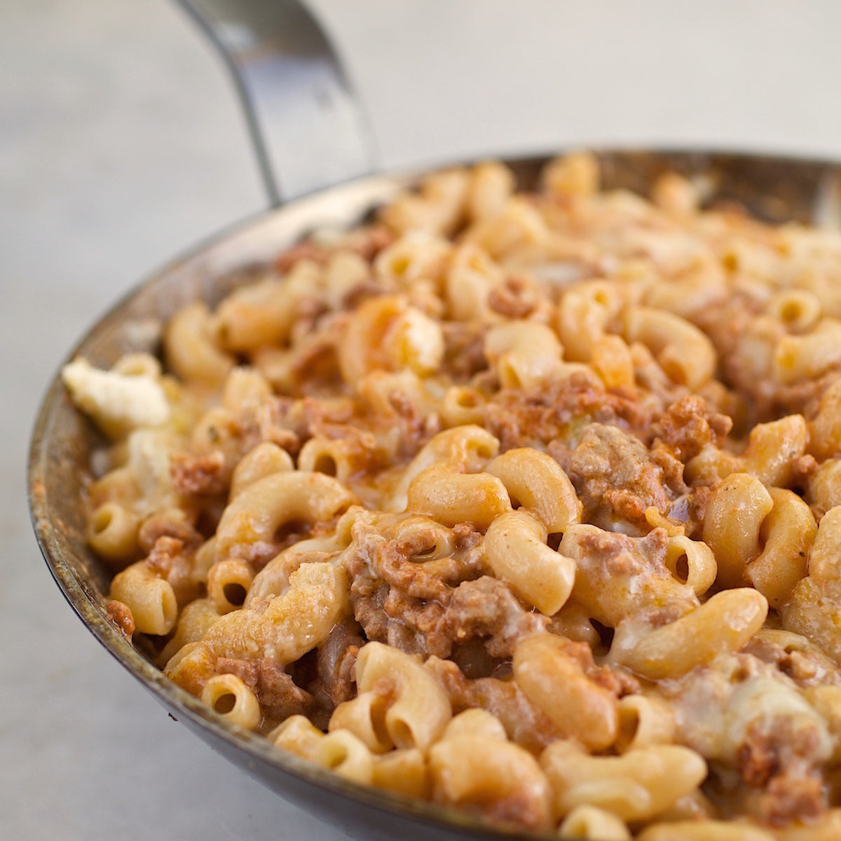 Close-up of Organic Gluten Free Brown Rice Elbows cooked in a skillet with meat sauce and melted cheese