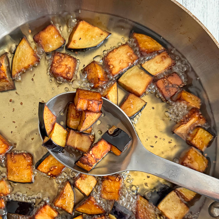 Browned eggplant cubes frying in olive oil in a skillet being lifted with a stainless spoon