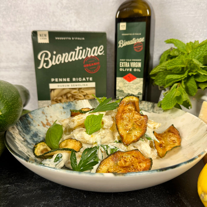 Penne with ricotta, lemon, herbs and fried zucchini in a bowl, with Bionaturae pasta box and extra virgin olive oil bottle behind