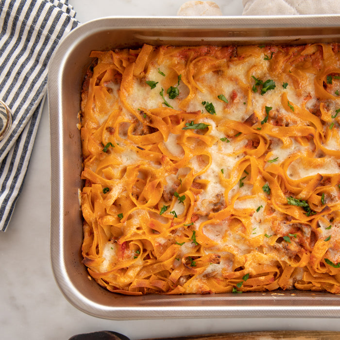 Gluten-free noodle casserole baked in a rectangular pan, topped with melted mozzarella and chopped parsley