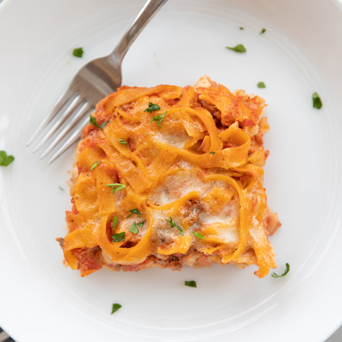 Gluten-free Italian noodle casserole square with melted cheese and parsley on a white plate with a fork