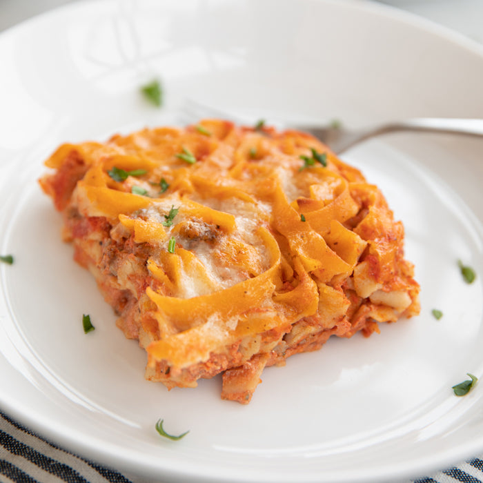 Slice of gluten-free noodle casserole with tomato sauce, melted mozzarella and Pecorino, garnished with parsley served on a white plate