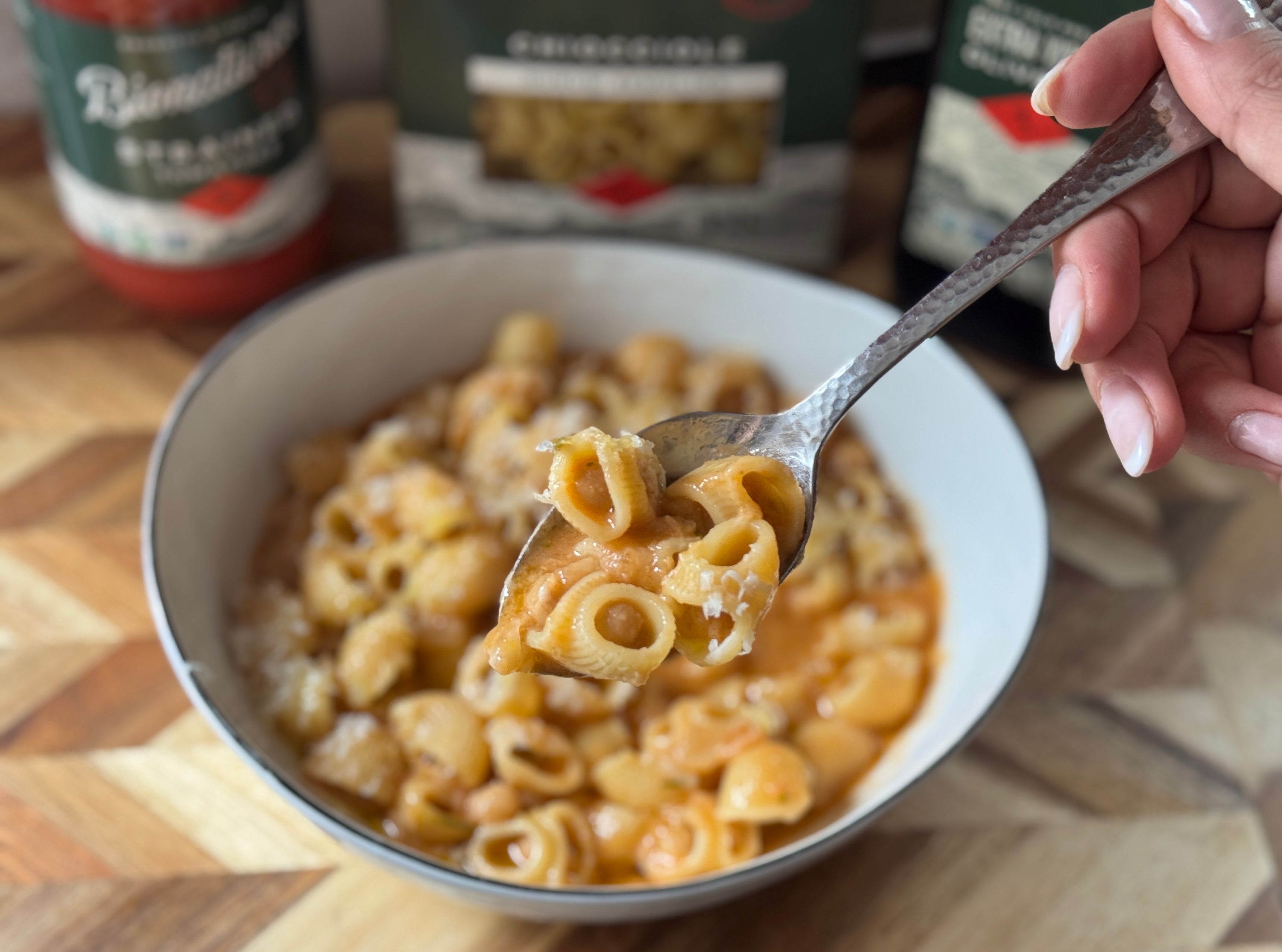 Chiocciole pasta and chickpeas lifted on a fork from a bowl on a wooden countertop with jars in the background