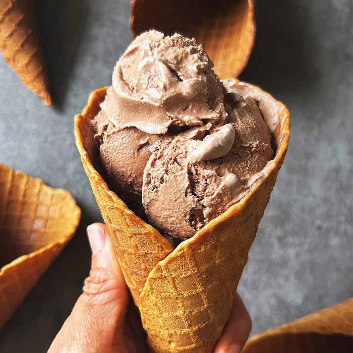 Close-up of handheld Einkorn sourdough waffle cone showcasing three scoops of chocolate ice cream against a gray background