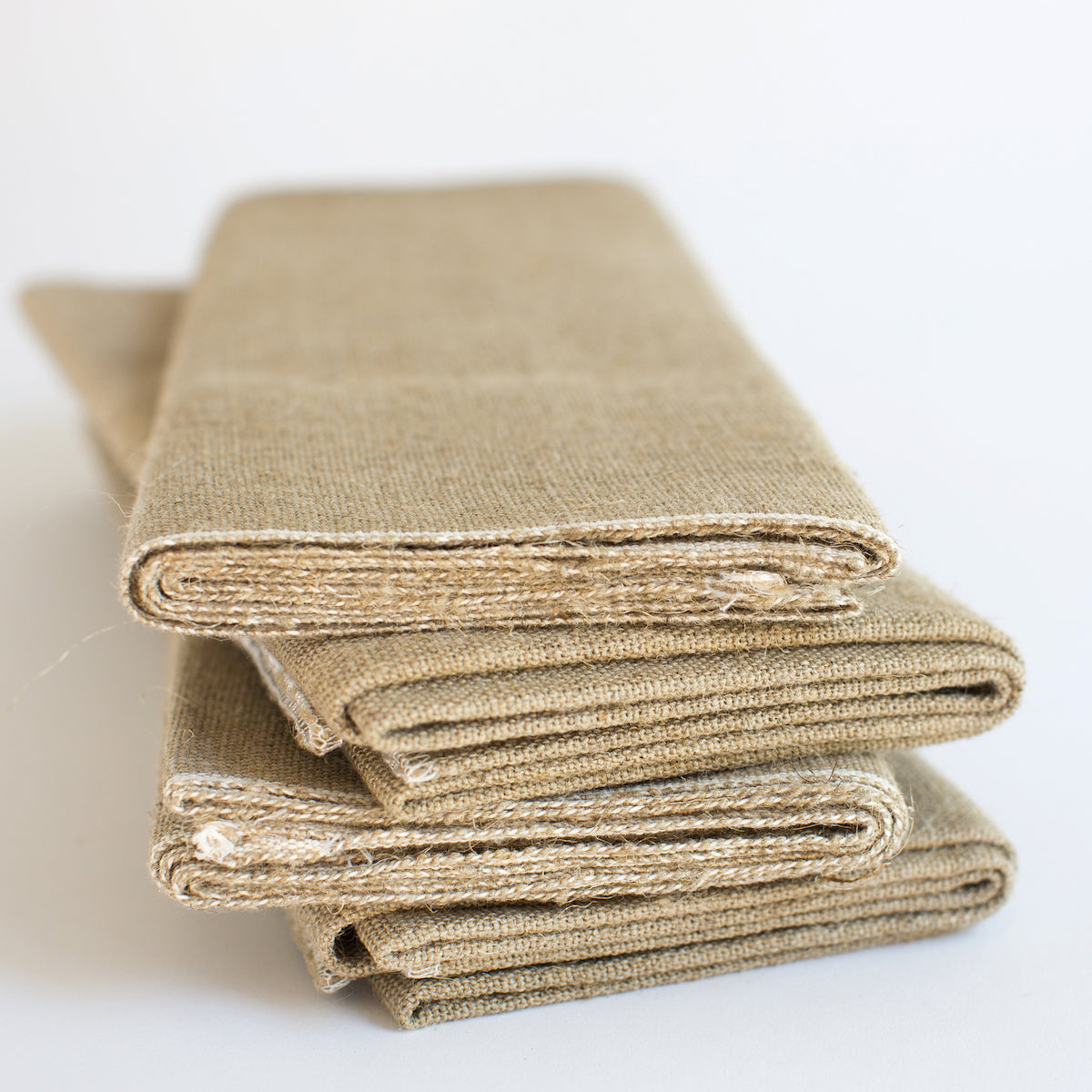 Close up of folded linen couche showing natural tan unbleached texture and tight weave on white background