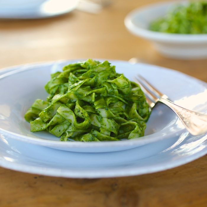 Fettuccine pasta tossed in bright green kale pesto, served on a white plate with a fork on a wooden table